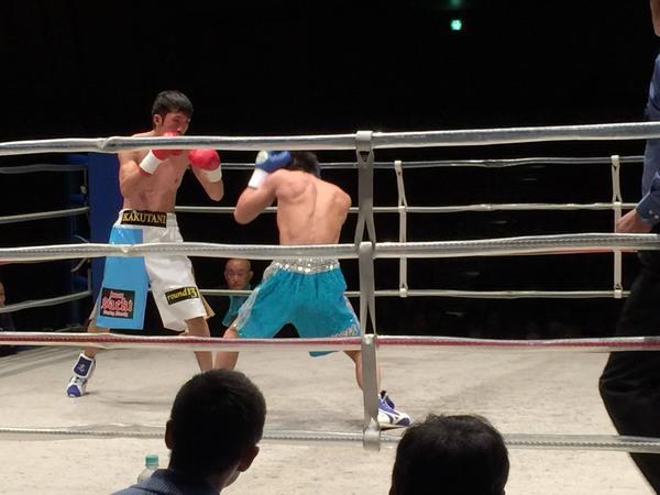 角谷 淳志選手がこぶしを顔の前で構えて,油田 京士選手が両手で顔を防御している様子の試合の写真