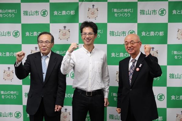 篠山市民ランナーの山下 八寿男さんと西口 昌宏さんと市長が片手ガッツポーズをして一緒に記念撮影している写真