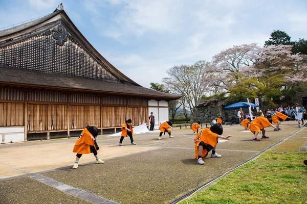 篠山城 大書院の前でオレンジ色の法被を着た子ども達が、右手を伸ばし、下を向いて構えてポースを取っている様子の写真