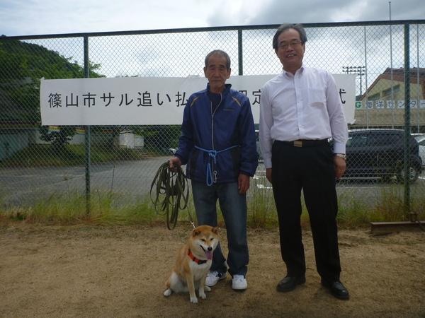 犬を連れた青いジャージ姿の男性と副市長が並んでいる写真