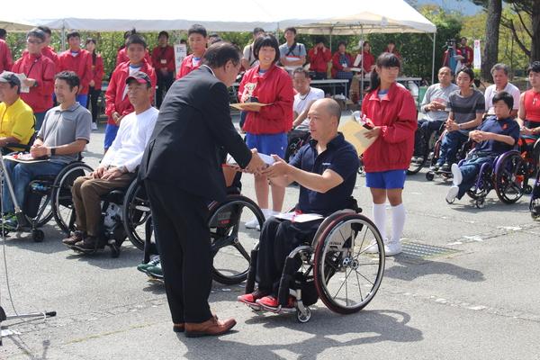 車いすのランナーがスーツを着た男性から記念品を受け取っている写真