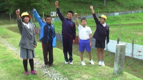 農道で小学生男女5名が右手を挙げて笑顔で写っている写真