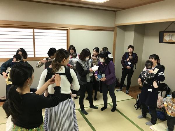 背中の留め金を取り付けてもらったり、赤ちゃんを抱っこひもで前に抱いたりして赤ちゃんの様子をお母さん達が確認している様子の写真、