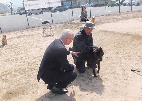 空き地で男性の連れた犬の体を市長がなでている写真