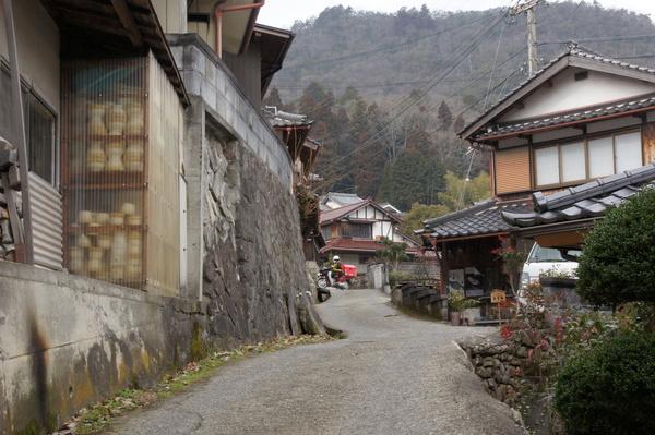 坂の途中に家々が立ち並び、遠くには山並みが広がっている風景を坂道の下から見ている写真