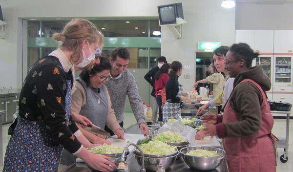 外国の方達がキャベツを切って料理を習っている写真