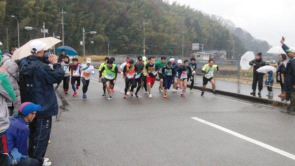 雨の中、傘をさして応援する観客の中、スタート地点から走り出す、篠山市新春駅伝大会の参加者の写真