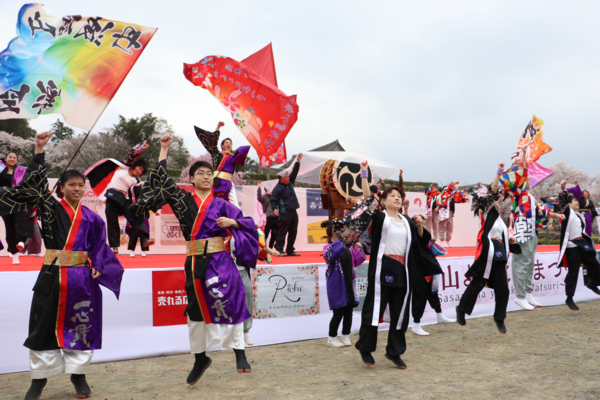 ステージ上で踊る人達、右手で握り拳を作り手を挙げステージ上の前でジャンプをしているダンサーたちの写真