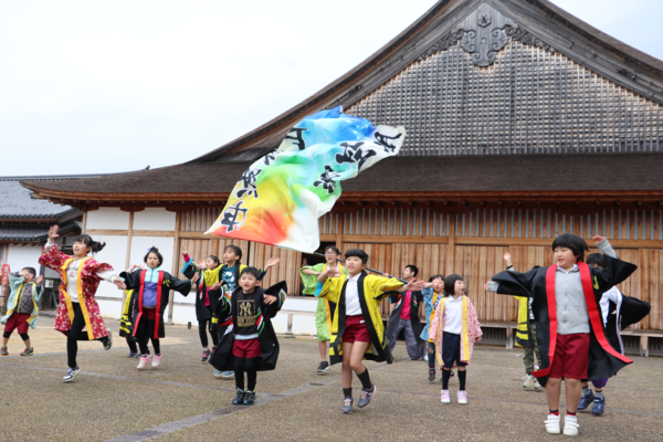 篠山城大書院の前で一人が大漁旗のような大きな旗を振り、約11人の子供たちがはっぴを着て踊っている写真