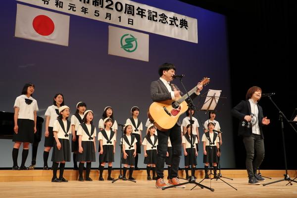 ちめいどの二人がギターとタンバリンを使いながら歌っている後ろで、篠山少年少女合唱団も歌っている写真