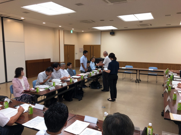 向かい合わせに長机に座って行われている会議中に市長が書類を渡している写真