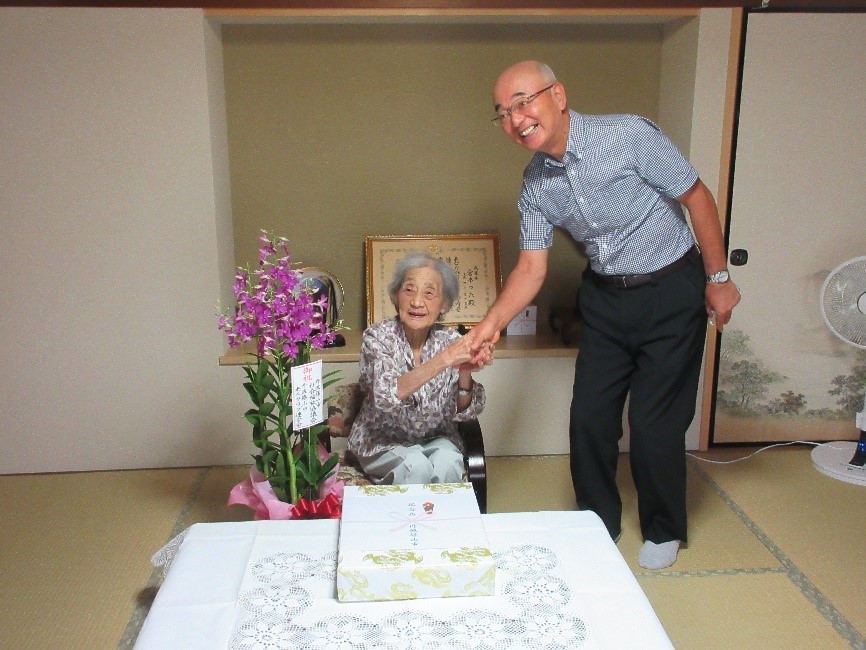 椅子に座っている宮本さんと、市長が握手している