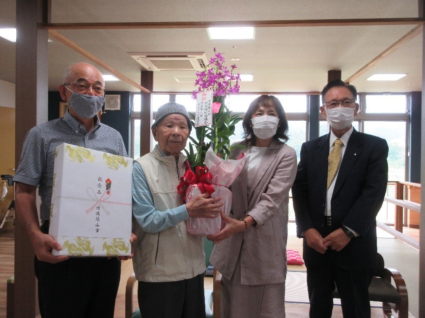 市関係者が波部さんに花束を贈呈している、隣で市長が記念品を持っている