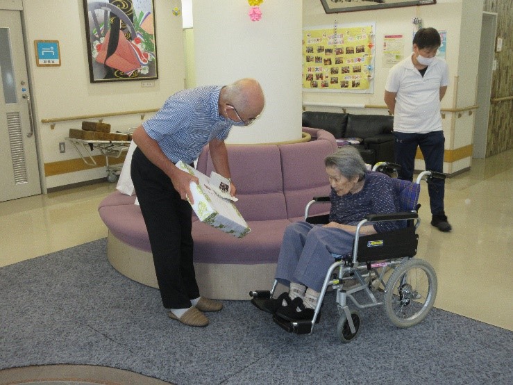 車いすに乗られている前川さんに市長が記念品を贈呈している
