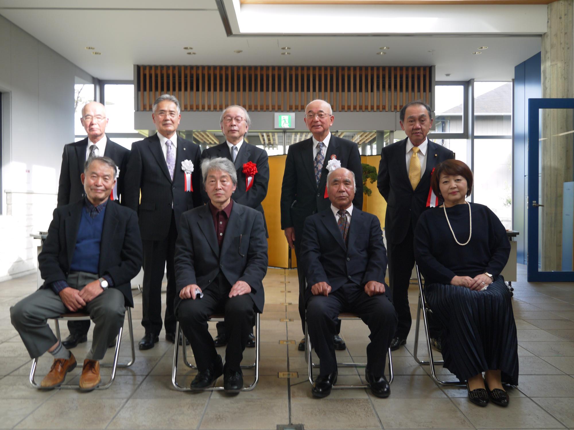 市展に入賞された皆さんが椅子に座り、後ろに関係者の皆さんが立っている。