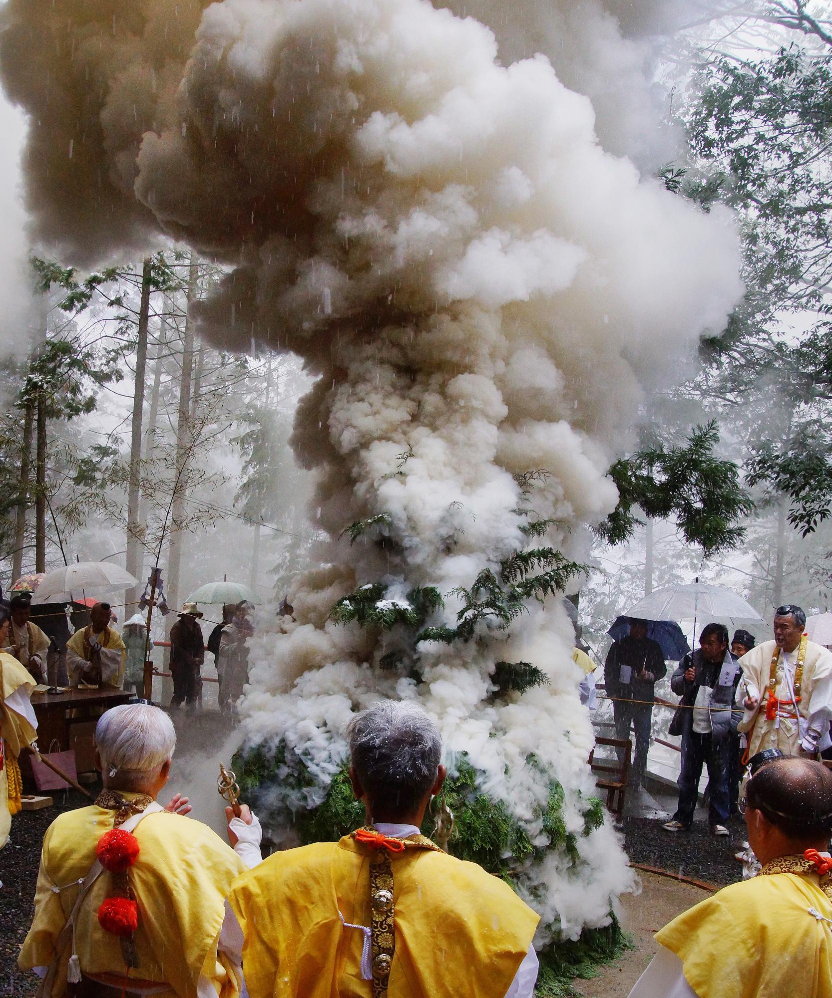 雨の中護摩焚きをしており、煙が空に向かってのびている。