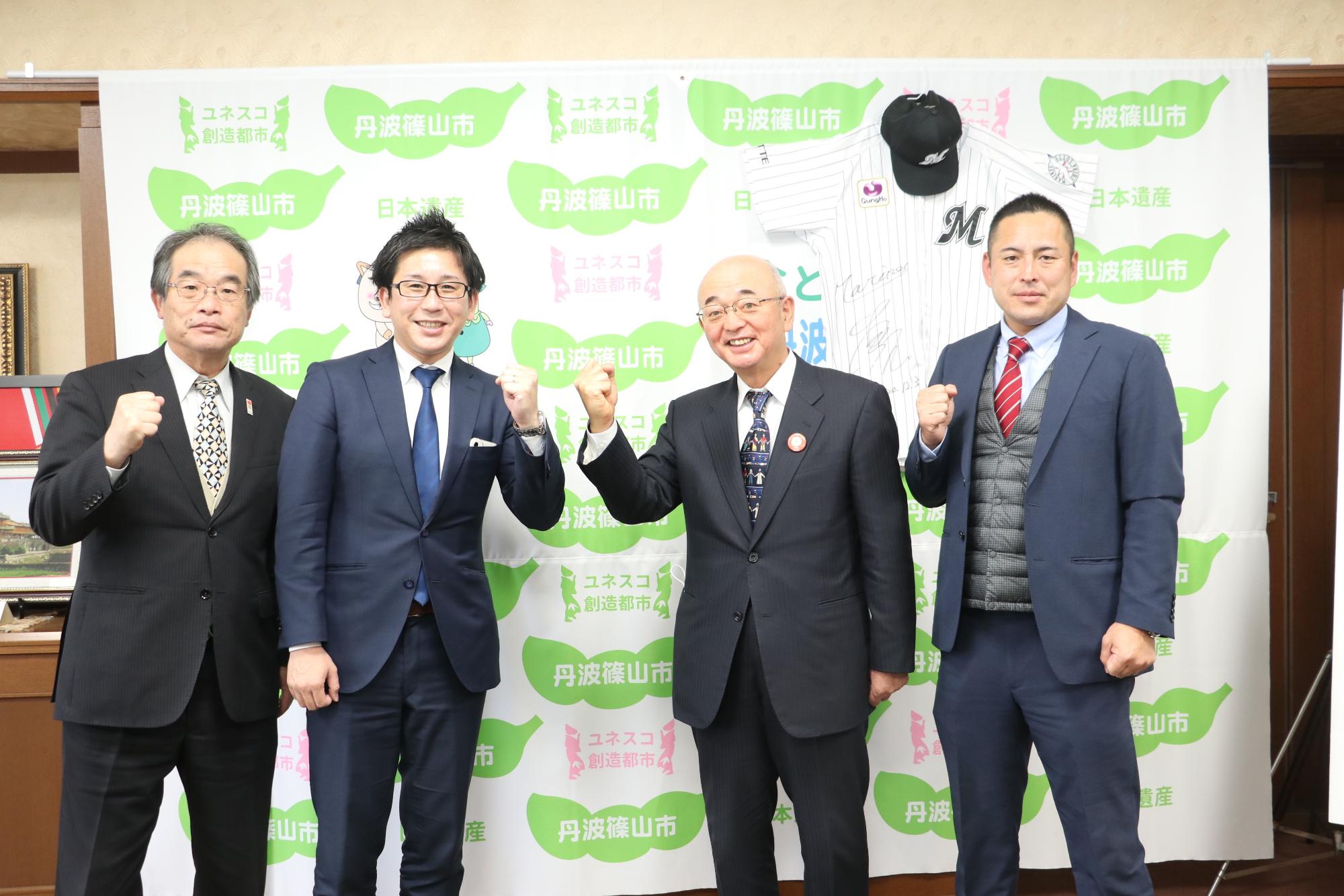 千葉ロッテマリーンズのユニフォームと帽子をタペストリーに掛けて、大石さん、市長、副市長、担当職員が記念撮影