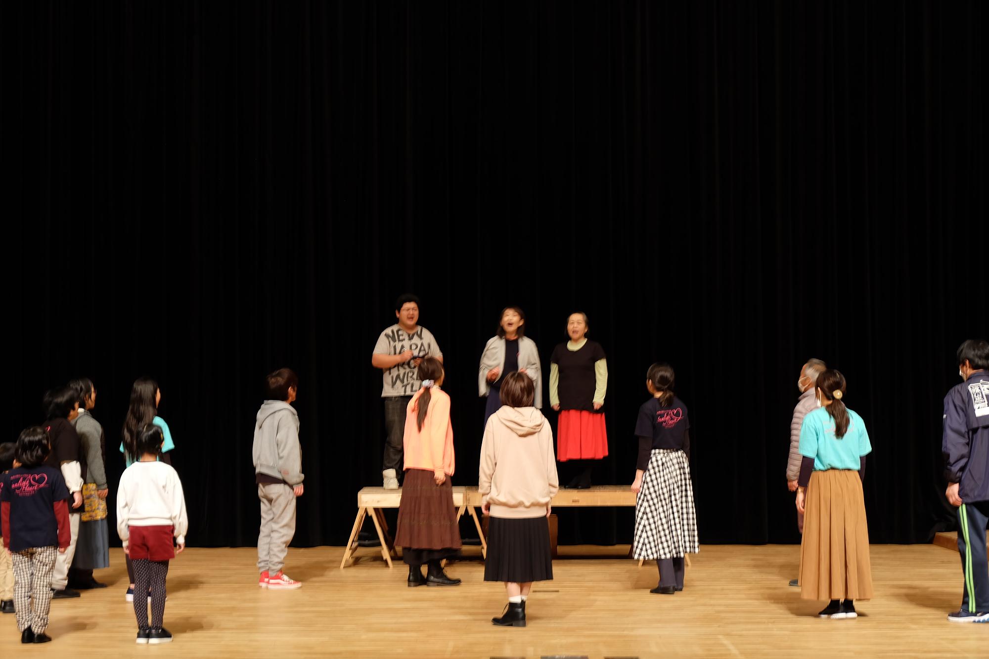 少し高さの高いところに3人の人が立って前に向かって話しており、それを下から見上げる複数の出演者の方の写真