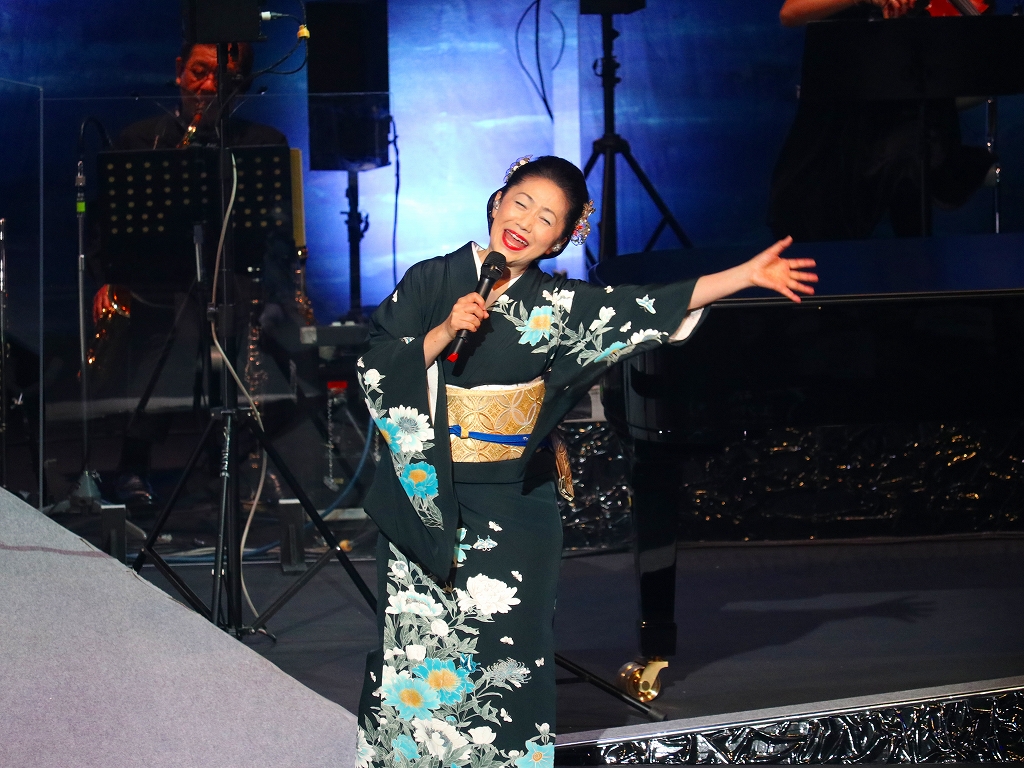 着物を着た女性がマイクを片手に歌っている。