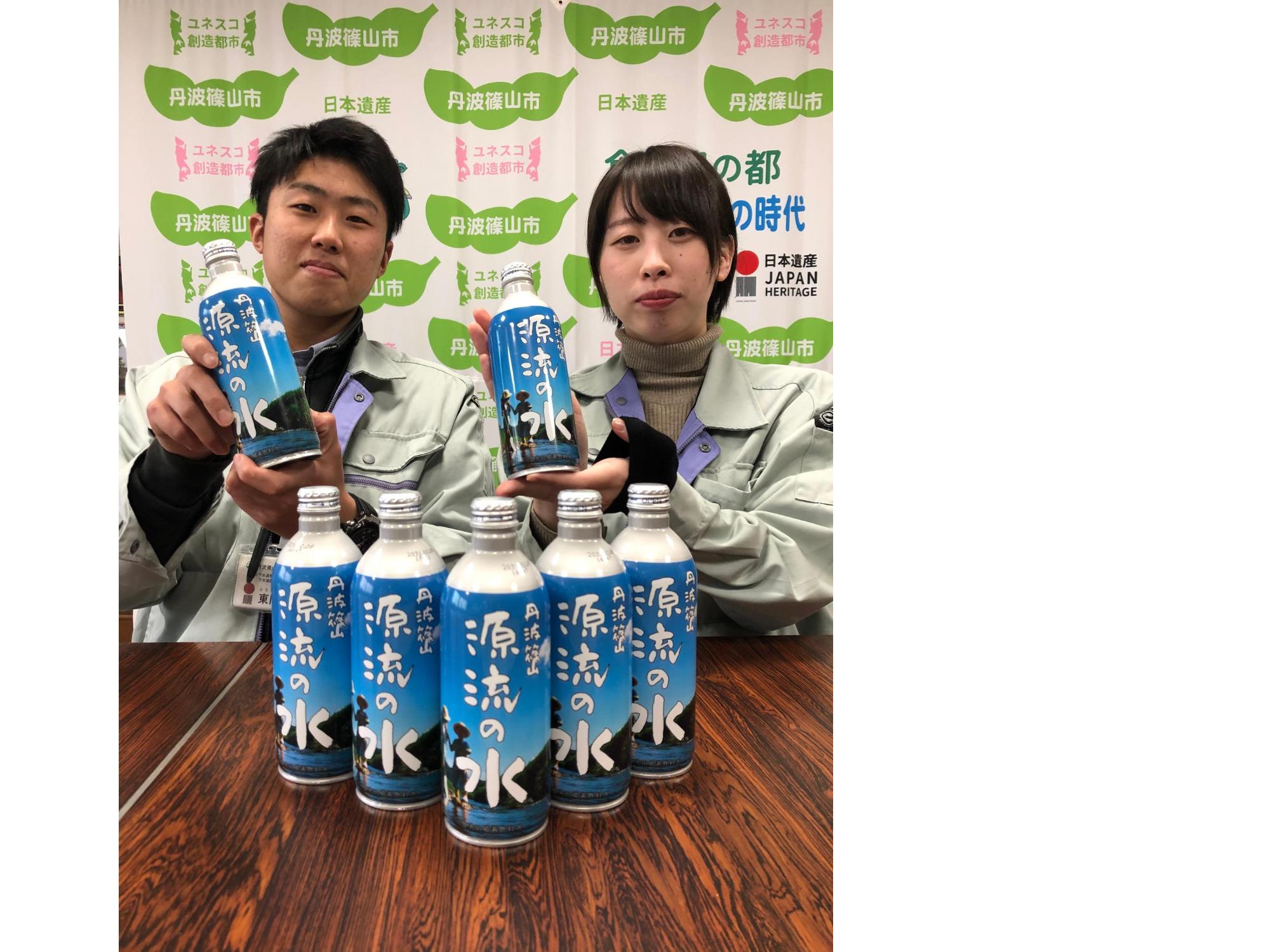 職員二人が手にボトルを持って記念撮影。机の上に保存水をボトルを並べてある。