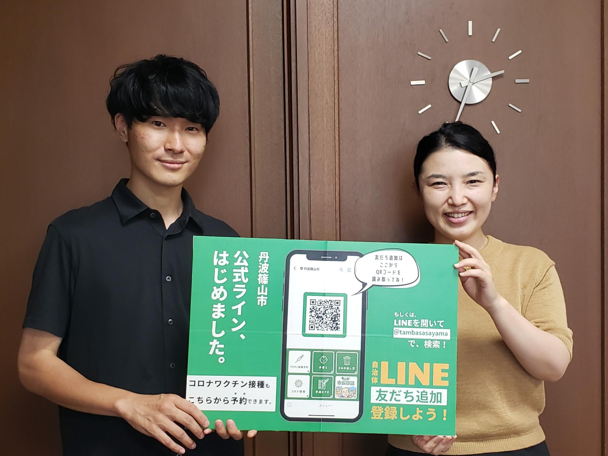 市が公式ラインをはじめたたPR看板を手に持った男性職員と女性職員
