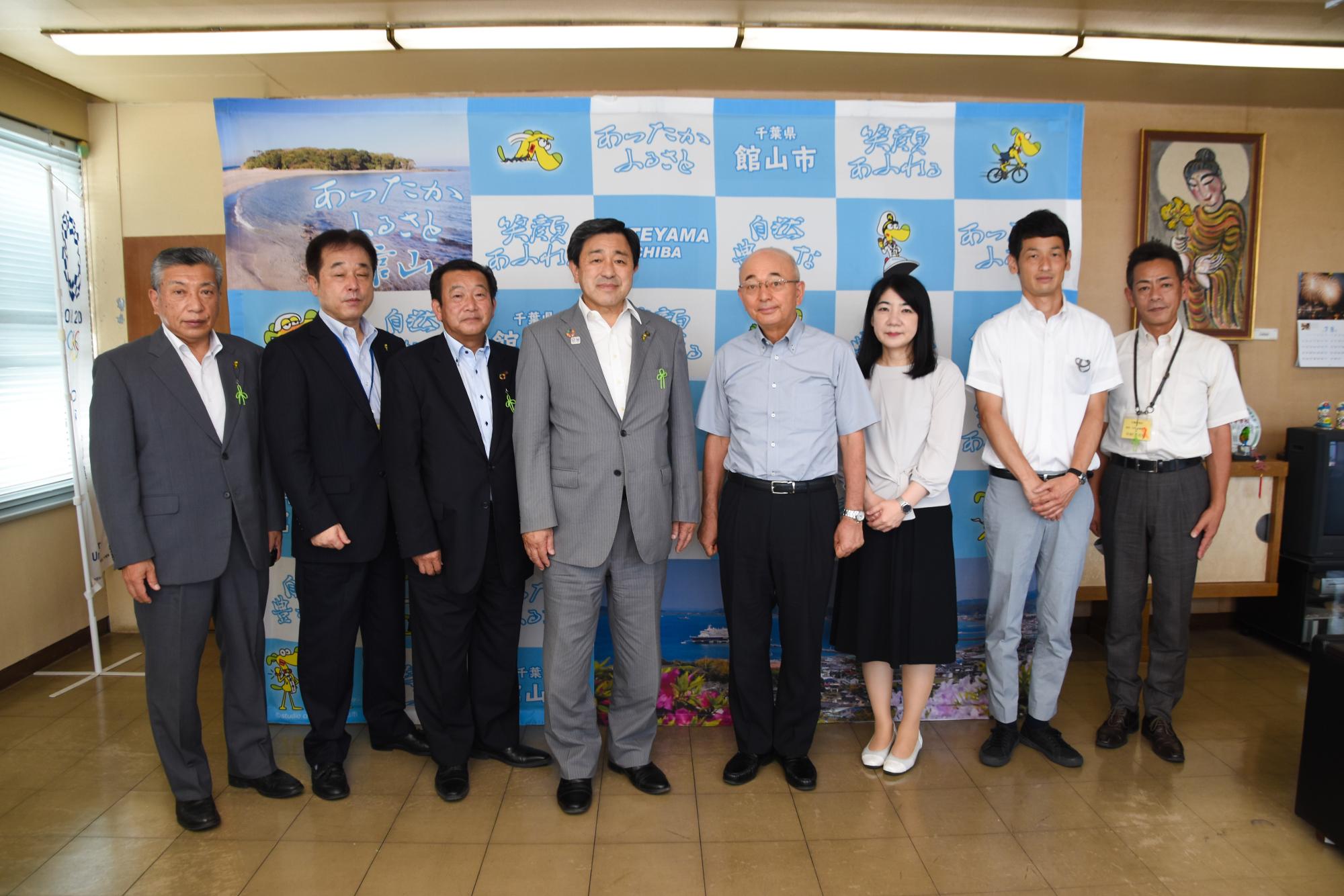 館山市のパネルの前で、館山市の教育長、副市長、市議会議長、市長、丹波篠山市の市長、職員が立って並んでいる。