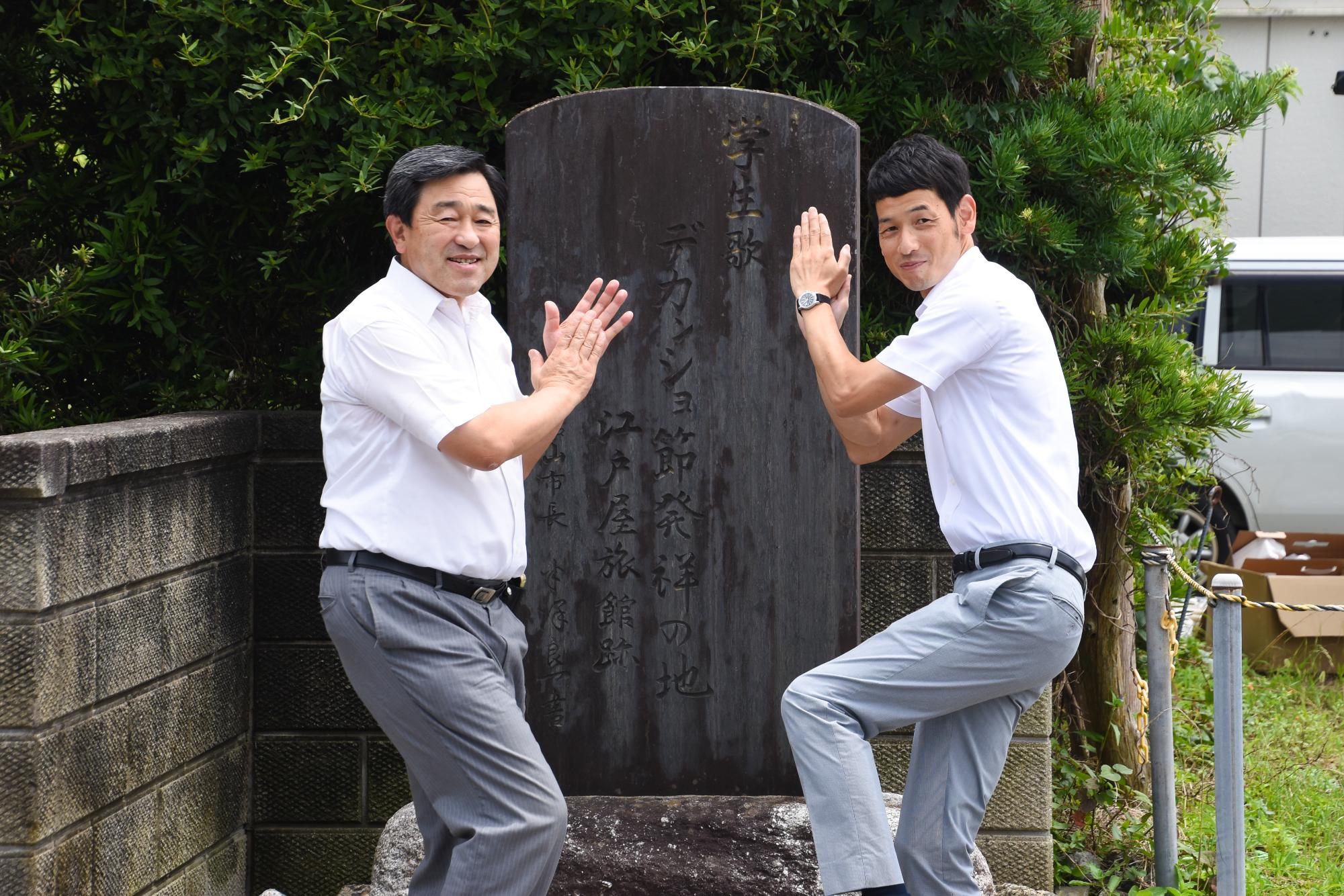 館山市のデカンショ発祥の碑の前で、デカンショのポーズをとっている館山市長と篠山デカンショ節保存会の職員