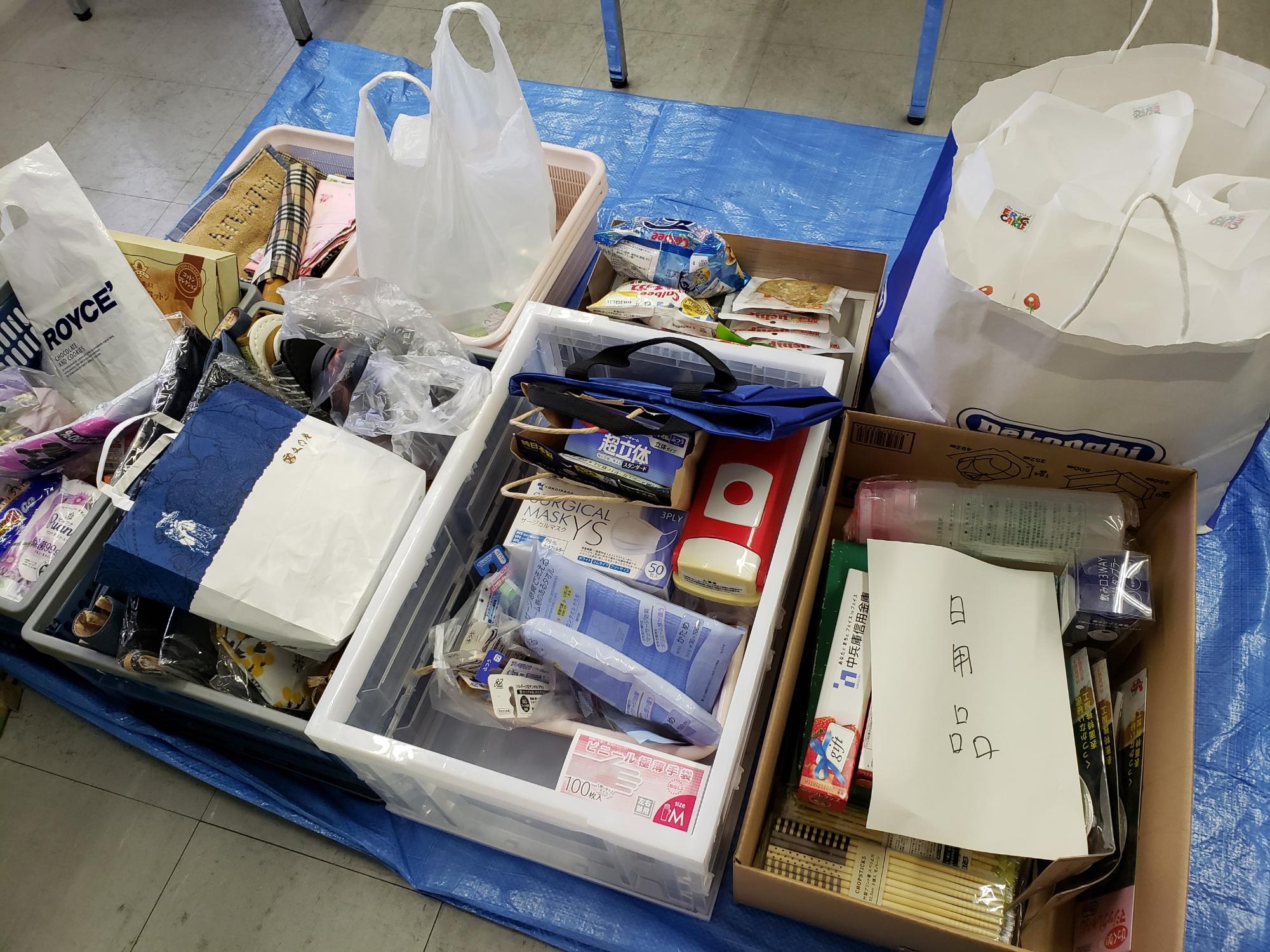 ブルーシートの上にコンテナが置かれており、日用品が入っている