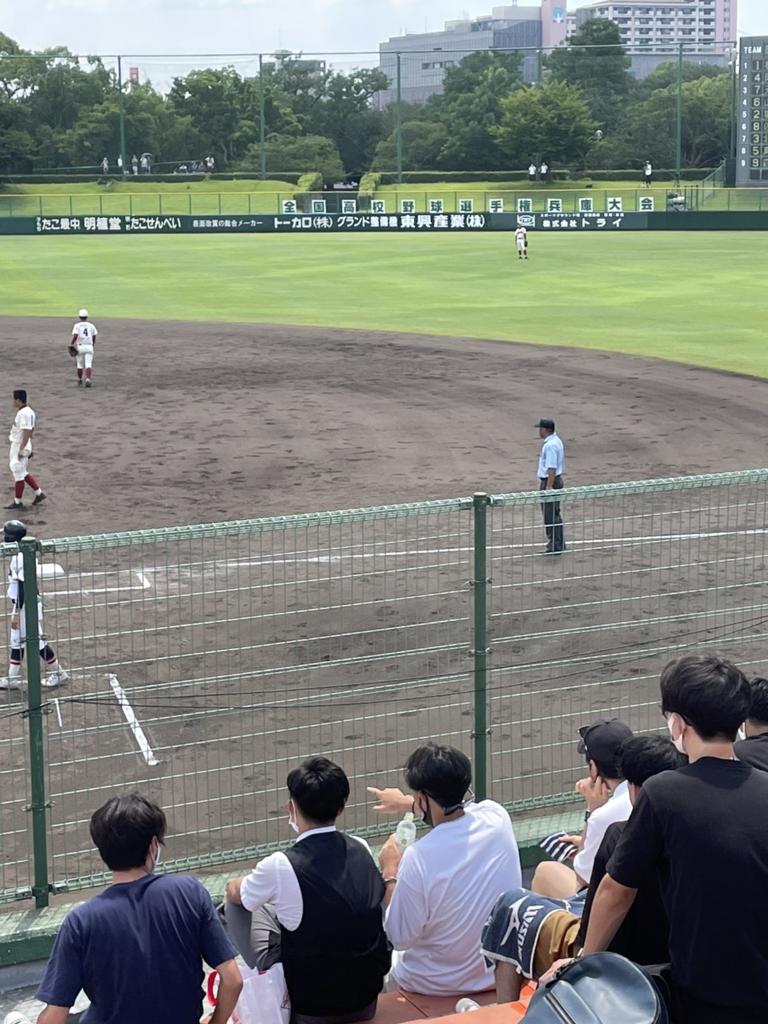 野球グラウンドで試合をしている。1塁のそばに審判が立っている。