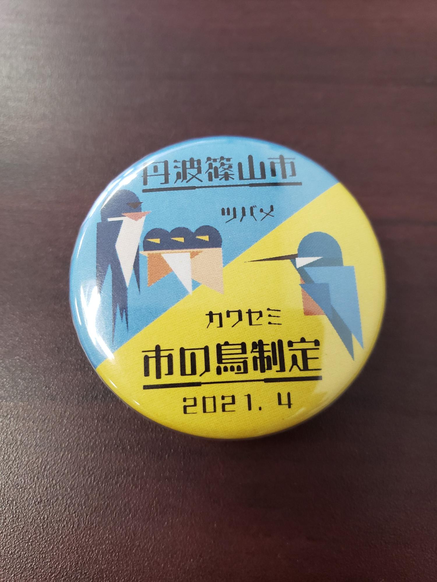 青と黄色のバイカラーを背景に、ツバメとカワセミのイラストが描いてある缶バッジ