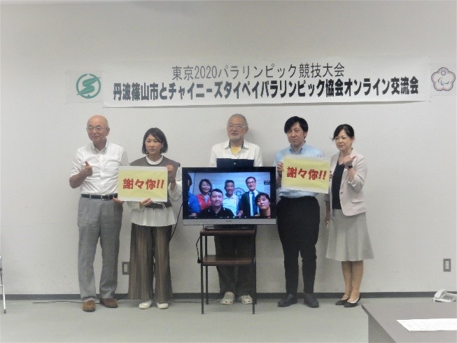 モニターのまわりにメッセージを書いたパネルを持った女性や男性、市長が立っている。