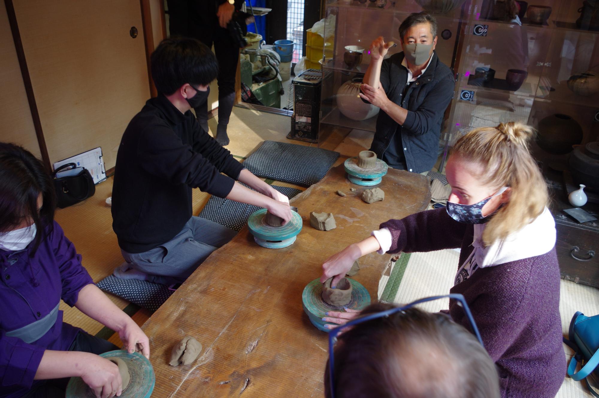 若い男女数名が陶芸体験をしていて、中央で先生が説明している