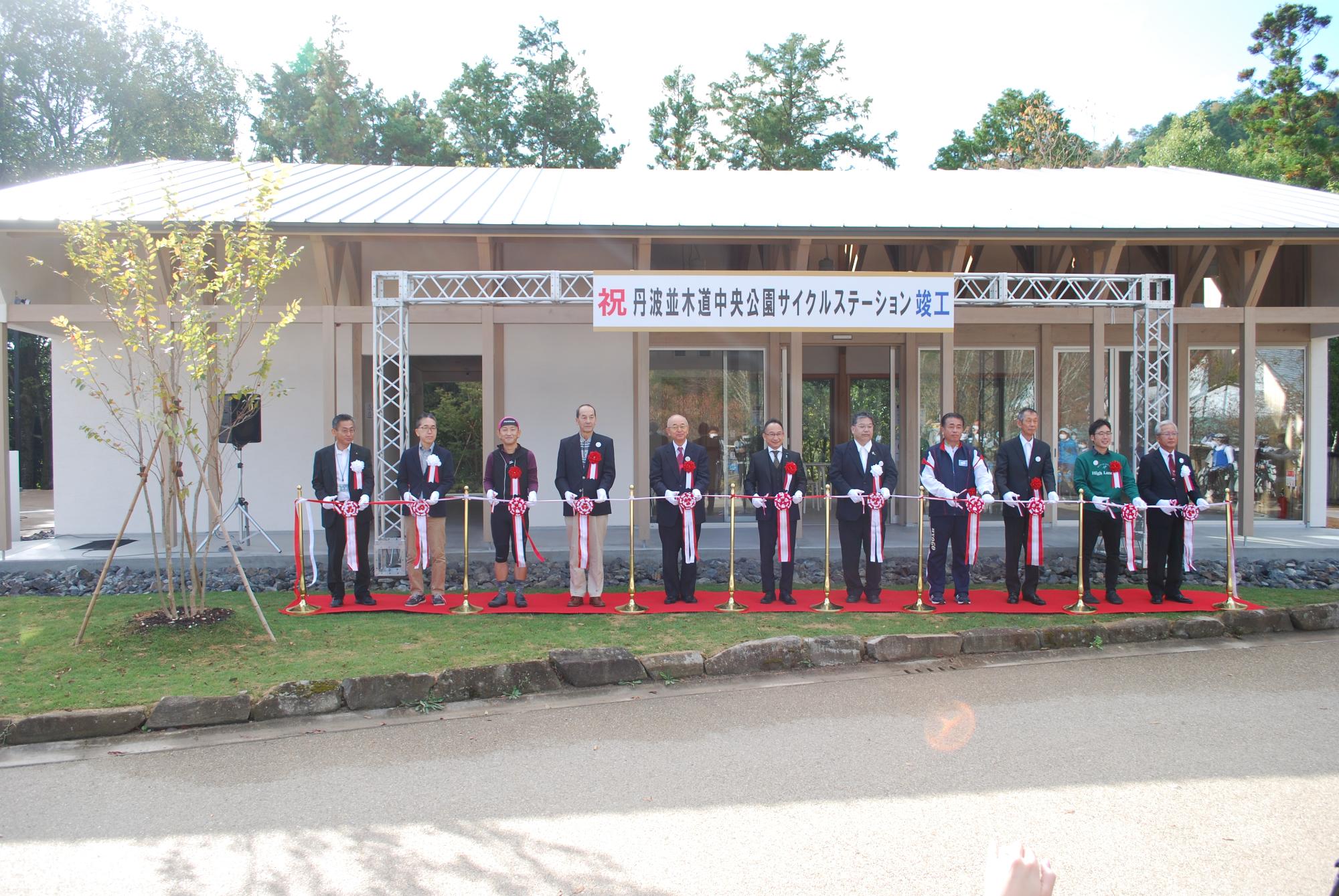 丹波並木道中央公園サイクルステーション竣工と書かれた横断幕の前で関係者がテープカットをしている