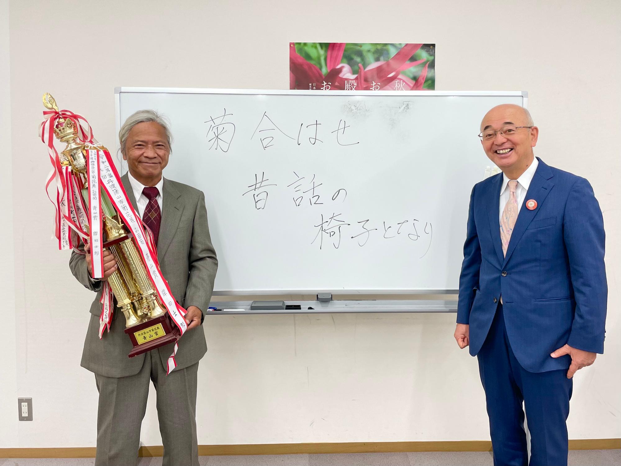 青山賞を受賞された男性がトロフィーを持ち、その隣に市長が立っている。
