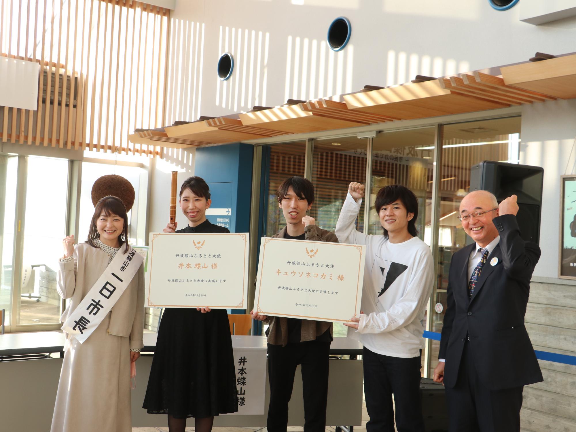 大きな委嘱状を手に持った井本さん、キュウソネコカミ、その隣に酒井市長と熊谷さんが並んで記念撮影