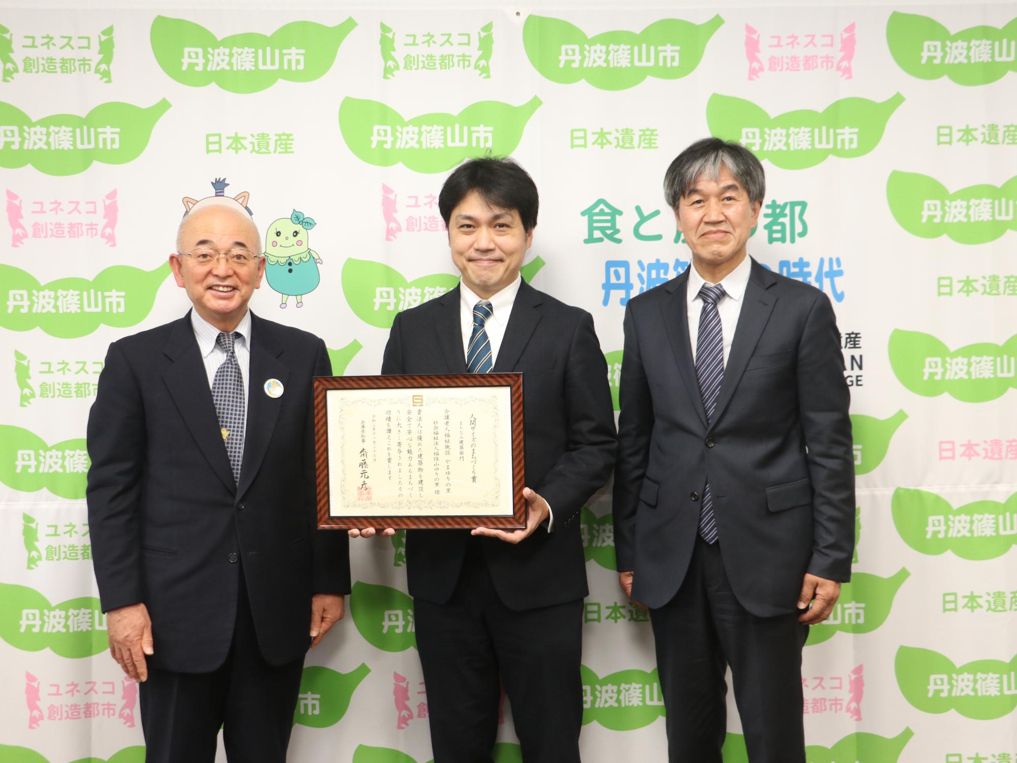 賞状を持った施設長と、設計事務所の方、市長との記念撮影