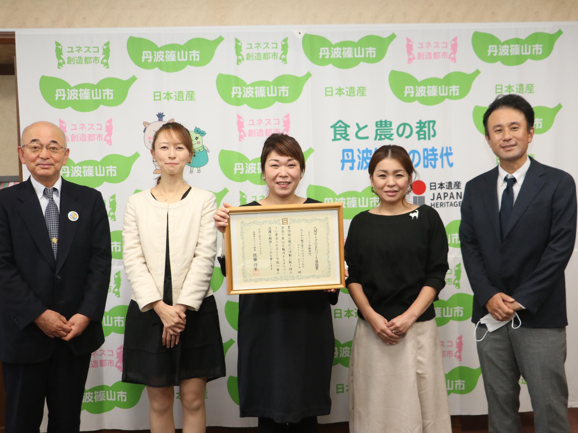 賞状を持った女性と、団体の関係者、市長との記念撮影