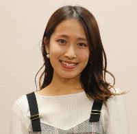 白い壁の前で、セミロングの女性が立っている