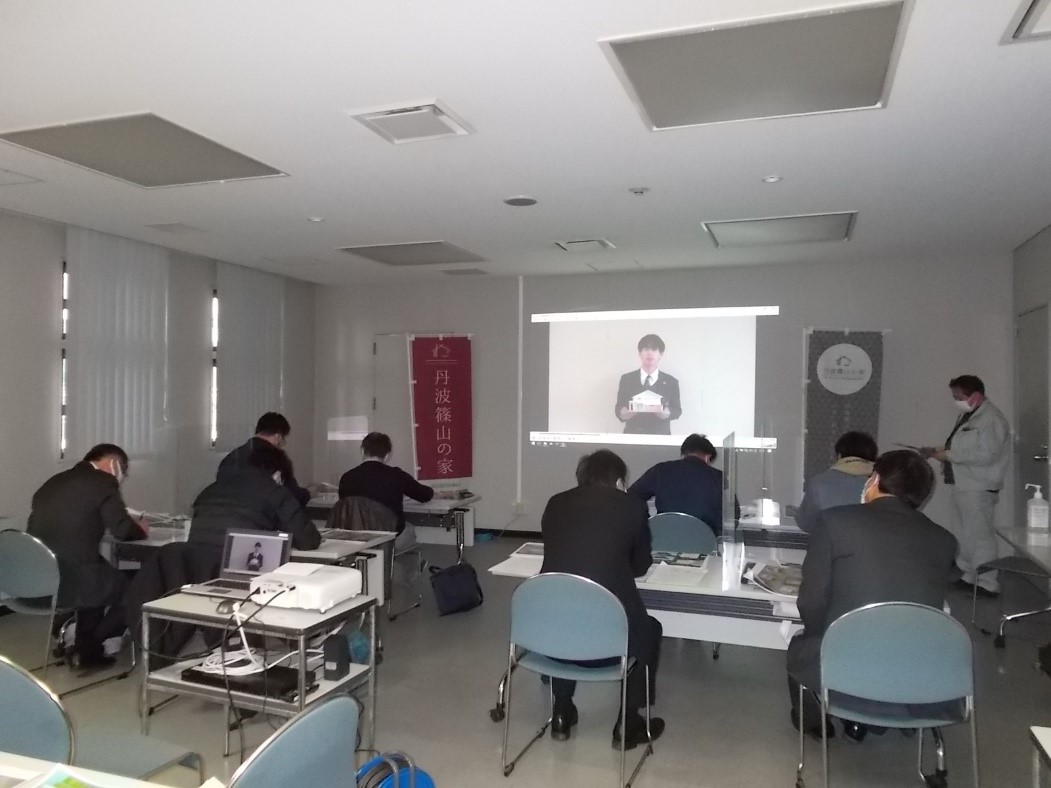 スライドに家の模型を持った学生が話している動画が流れていて審査員が聞いている