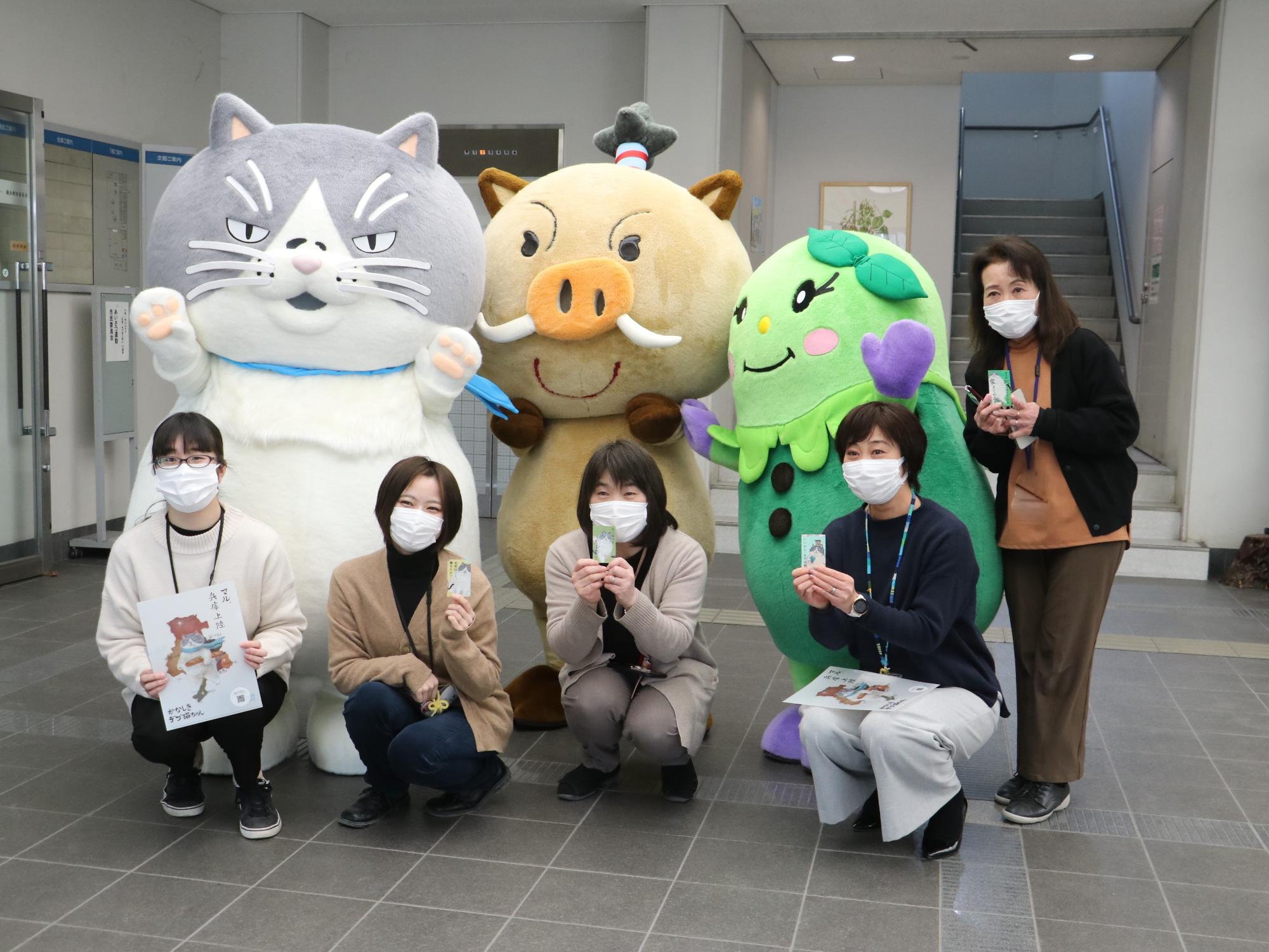 デブ猫マルとまるいのまめりんが後ろに立っていて、前列に市職員がいる