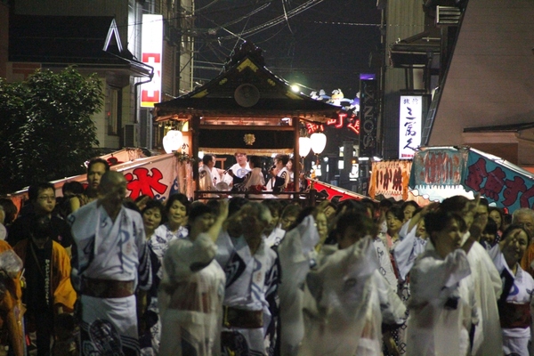 手前に踊り流をしている多くの人、奥に山車に乗ったお囃子の写真