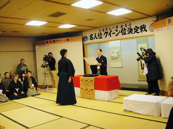 表彰を受ける岸田 諭名人をカメラマンが撮影している様子を正座して見ている袴姿の男性らの写真