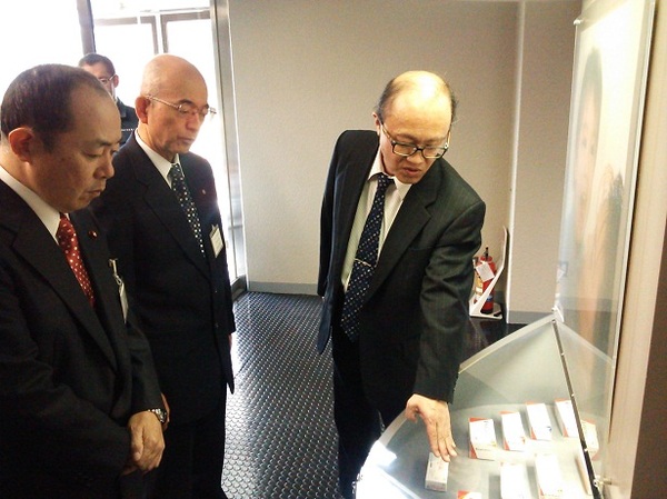 医薬品を手で紹介している山本工場長の説明を熱心にきいている男性2人の写真