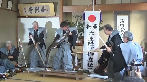 袴を着た男性たちが大蛇の作り物に木刀を向けて退治しようとしている様子の映像写真