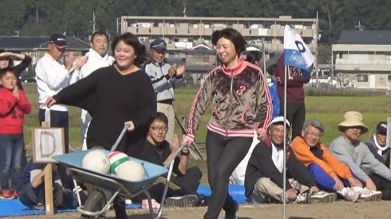 女性2名が一輪車を一緒に握りながら、その中のボールが落ちないように気にしながら走っている映像写真