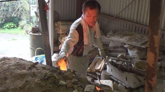 陶芸家 村上 登志男さんが窯に赤に熱を持った炭を入れようとしている映像写真
