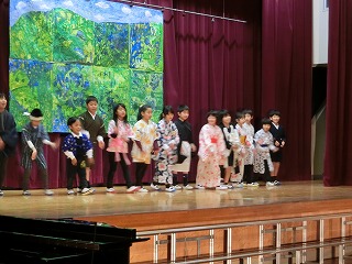 山と青い空を描いた絵を背景にして、和装をきた子どもたちが一列に並んでいる写真