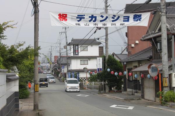 街に、祝 デカンショ祭の旗が飾られ、その下を通る車の写真
