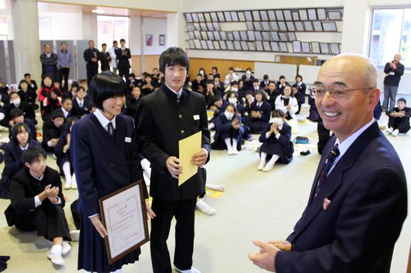市長の前で、恥ずかしそうに表彰状と黄色い紙を持っている男女の生徒の写真