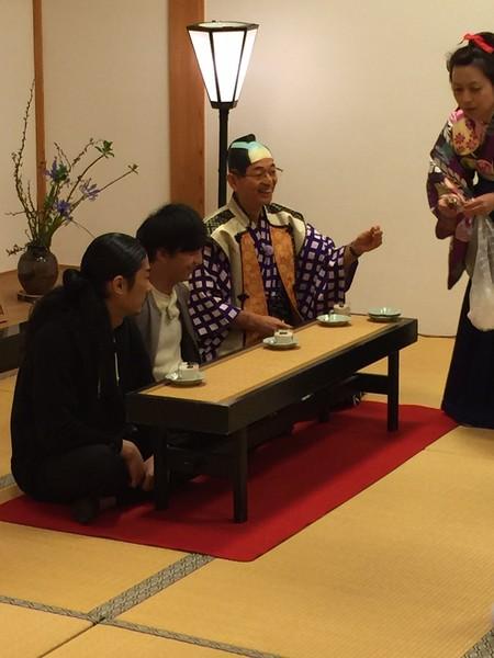 吉本の芸人2人と市長の前にお皿に入った豆腐が並べられていて女性がスプーンを配ろうとしている写真
